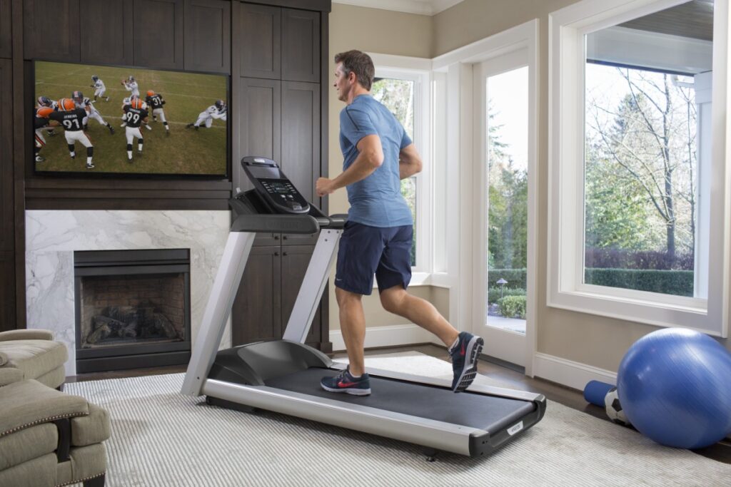A man runs on his Precor treadmill at home while watching a football game on TV. 