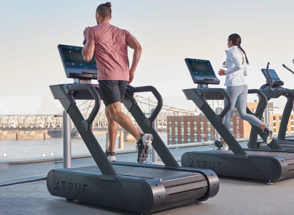 People running on TRUE Fitness Stryker Slat treadmills on a rooftop gym.