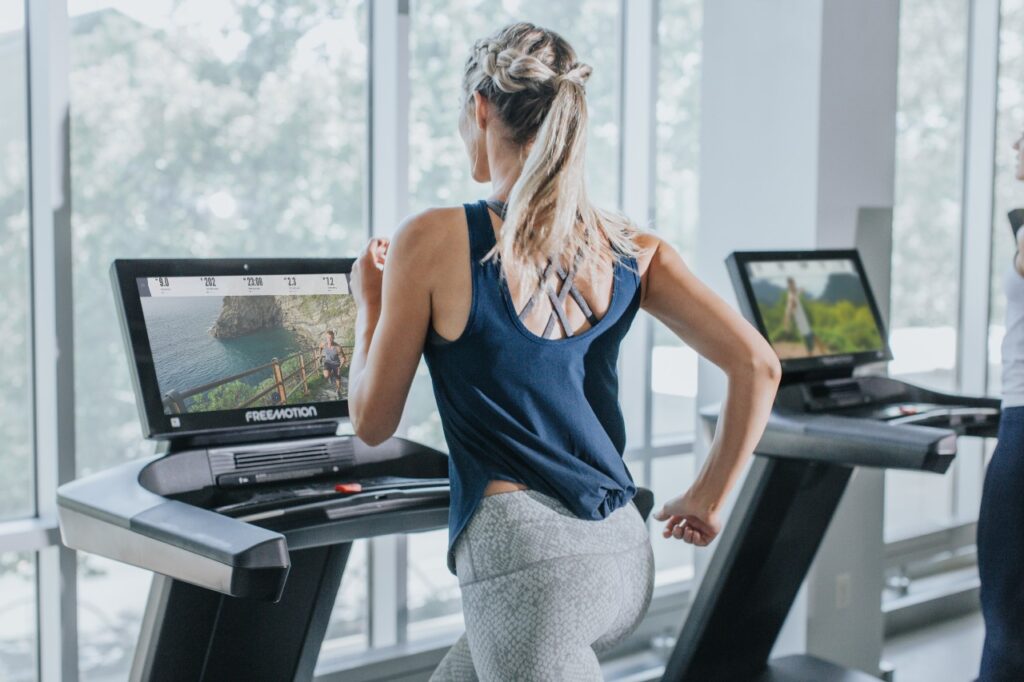 Closeup of a woman running on a Freemotion treadmill with 22-inch screen in a commercial gym. 